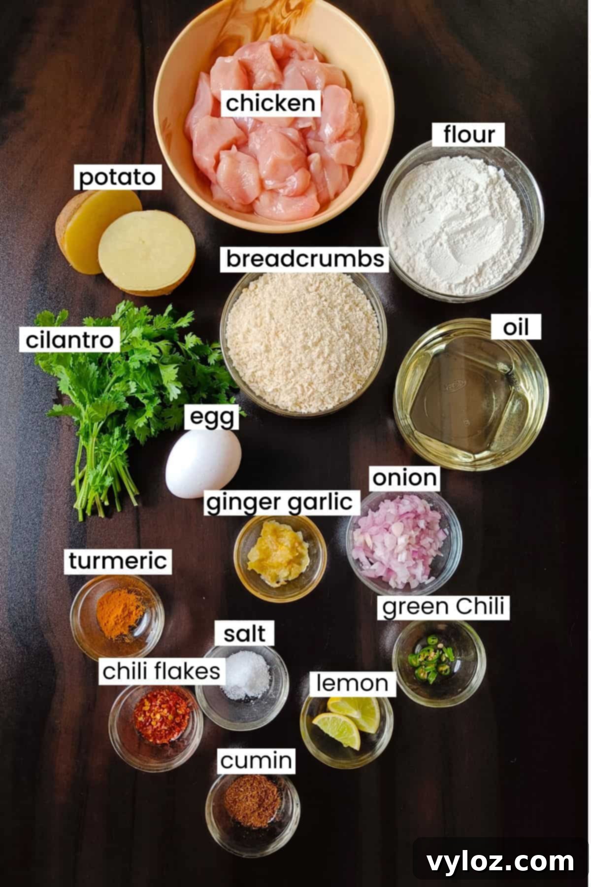 Ingredients for making chicken cutlets are placed on a dark brown background, showing fresh chicken, potatoes, spices, and coating elements.