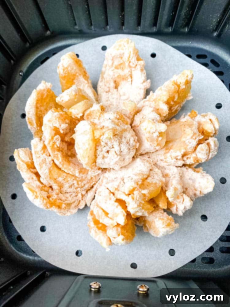 Restaurant-Style Air Fryer Blooming Onion 6 A partially cooked air fryer blooming onion positioned inside an air fryer basket, beginning to crisp up.