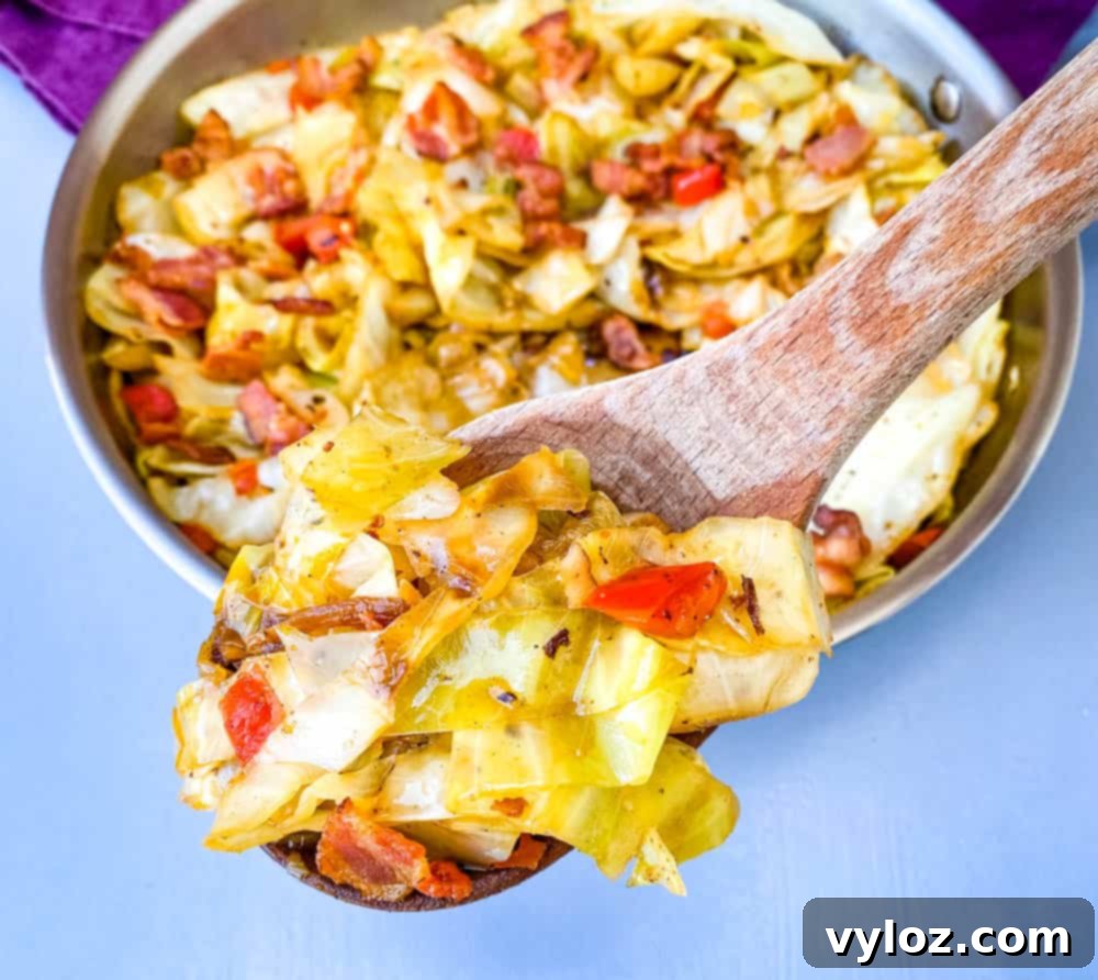 A generous serving of Southern fried cabbage with bacon, scooped into a wooden spoon, showcasing its tender texture and crispy bacon bits.