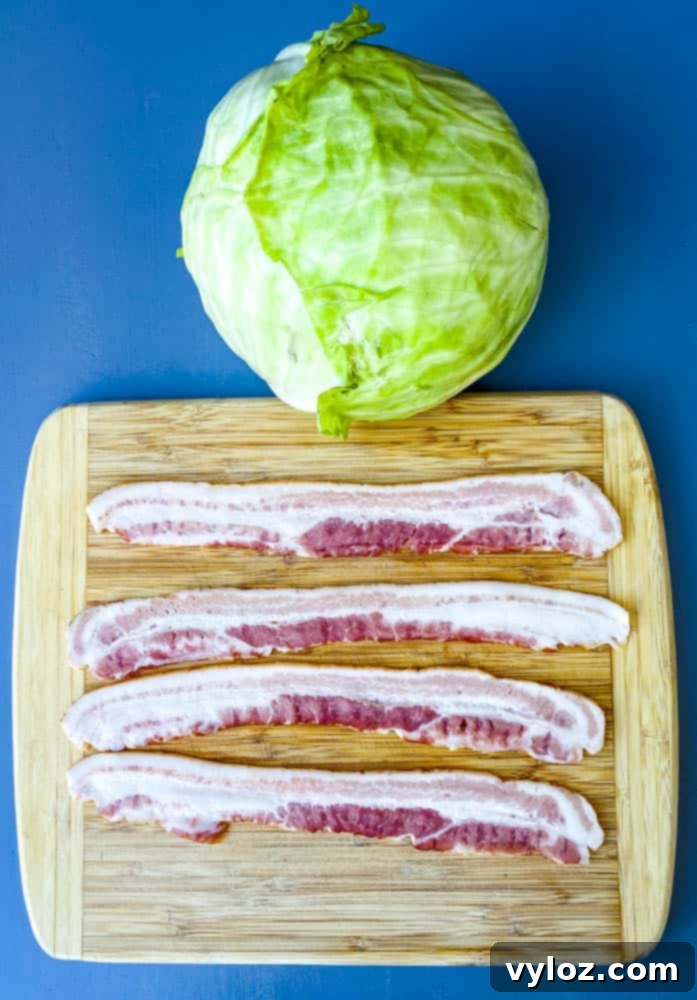 A whole, raw green cabbage head and several slices of uncooked bacon arranged on a cutting board, prepared for Southern fried cabbage.