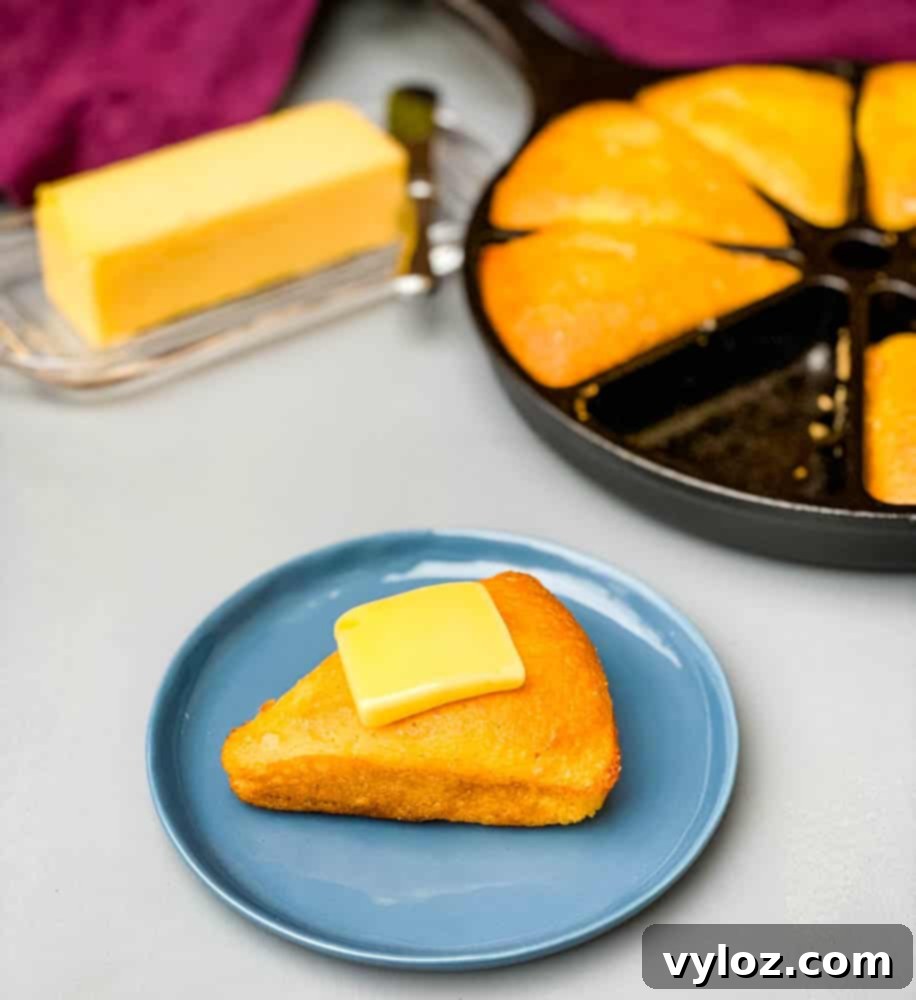 Keto low carb cornbread with butter on a blue plate with a cast iron skillet of low carb cornbread