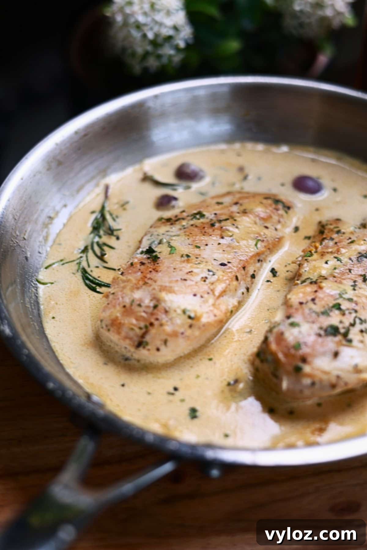 Chicken breasts with creamy garlic sauce in a skillet, garnished with fresh herbs.