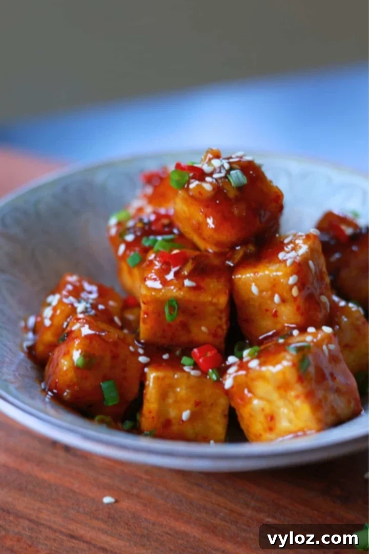 A bowl of honey garlic tofu with a glossy, flavorful sauce, garnished with sesame seeds and green onions.