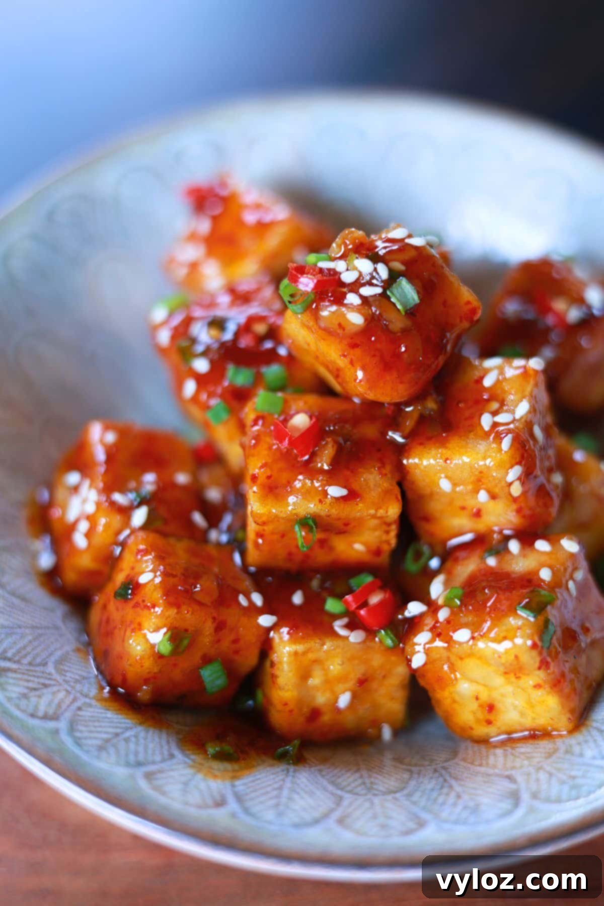 A bowl crispy tofu cubes coated in a  flavorful honey garlic glaze, topped with sesame seeds and green onions.