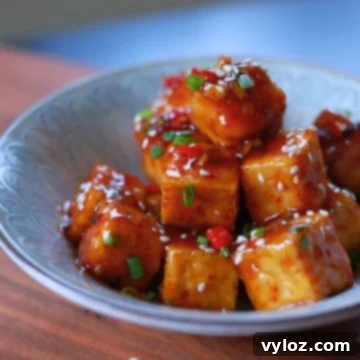 A bowl of honey garlic tofu with a glossy, flavorful sauce, garnished with sesame seeds and green onions.