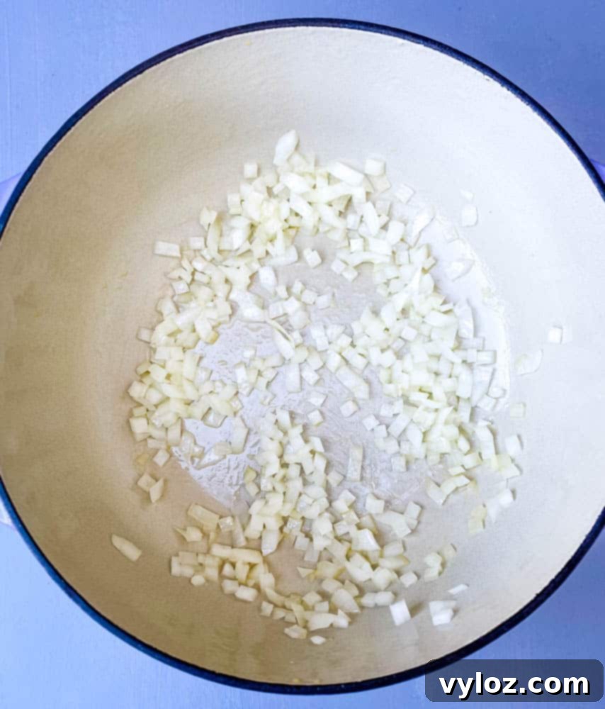Finely chopped onions sautéing in olive oil in a Dutch Oven, releasing their sweet aroma for the keto low carb marinara sauce.