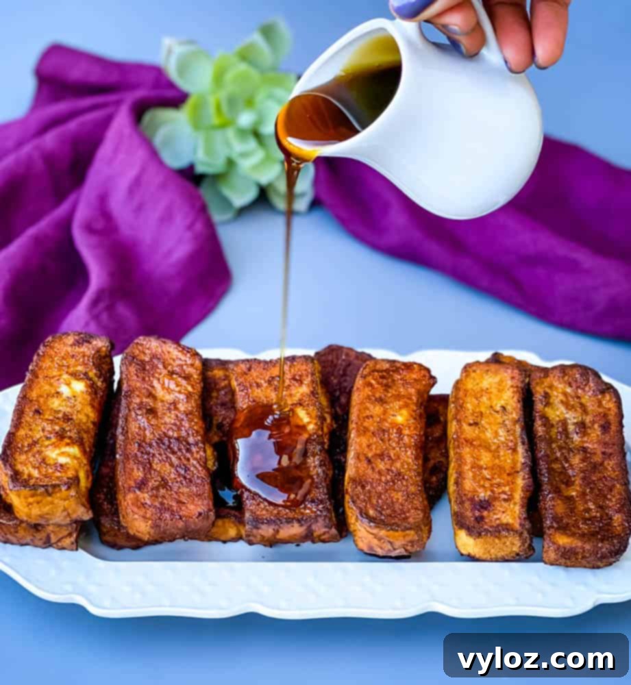 Delicious air fryer French toast sticks on a white plate, generously drizzled with sweet maple syrup