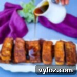 air fryer french toast sticks on a white plate with syrup drizzled throughout