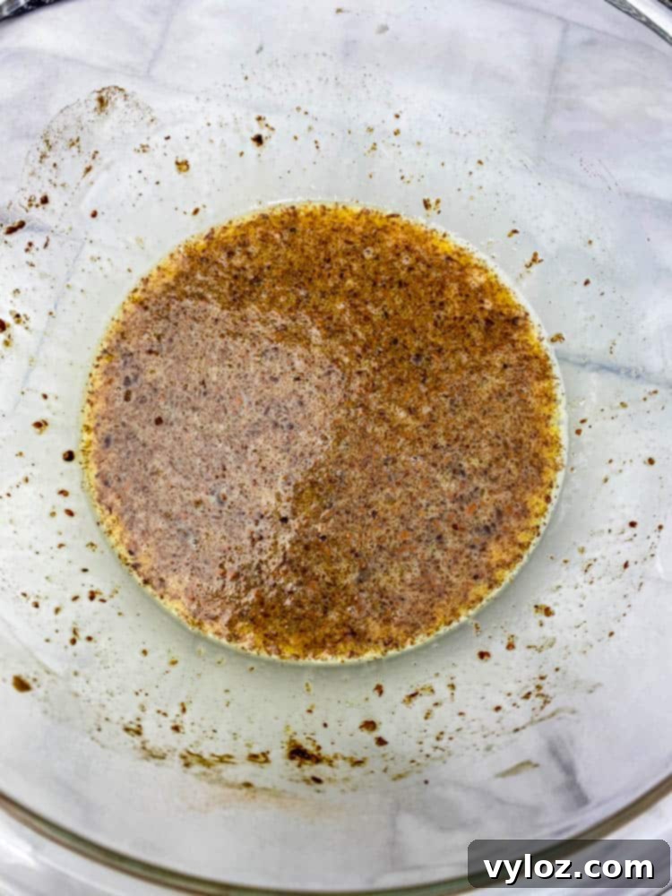 Close-up view of the smooth, golden-hued French toast batter in a transparent glass bowl, with a whisk resting inside, prepared for dipping bread sticks