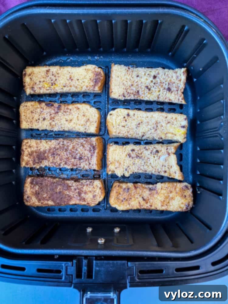 Uncooked French toast sticks meticulously arranged in a single layer inside an air fryer basket, poised for the cooking process