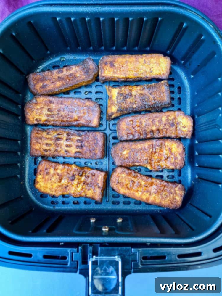 Golden-brown French toast sticks inside an air fryer basket, halfway through cooking, showcasing their even crisping and appealing color