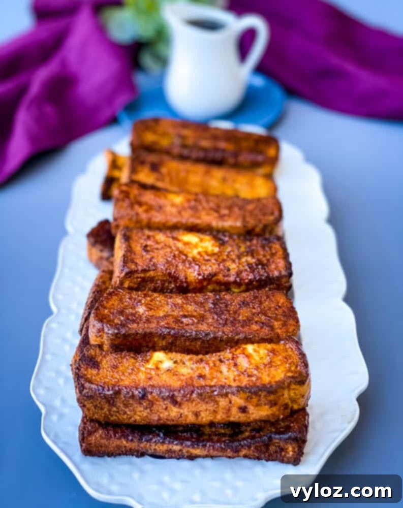 Freshly cooked, perfectly golden air fryer French toast sticks neatly arranged on a pristine white plate, prepared for serving