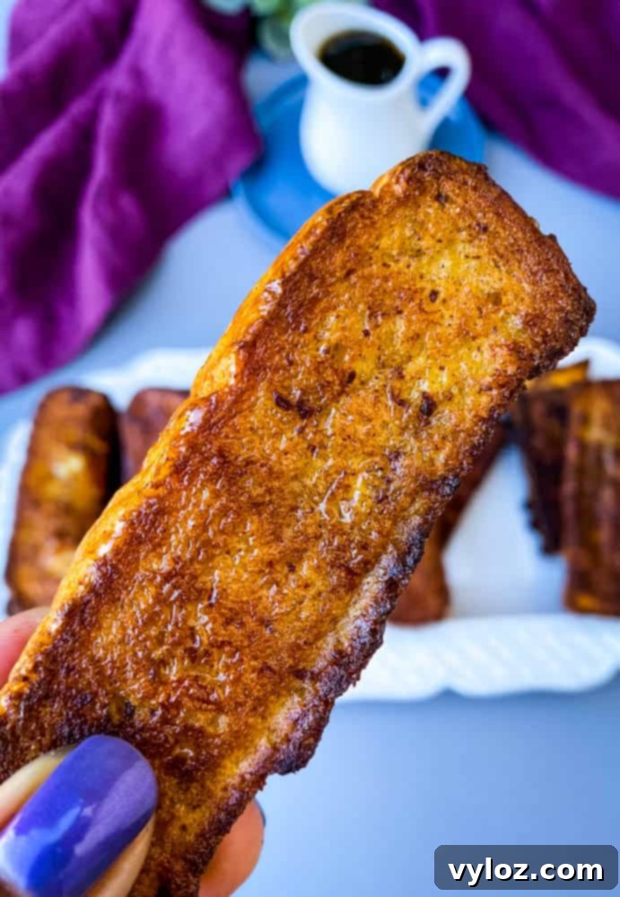 A hand reaching for a perfectly golden-brown air fryer French toast stick, highlighting its crisp texture and appealing look