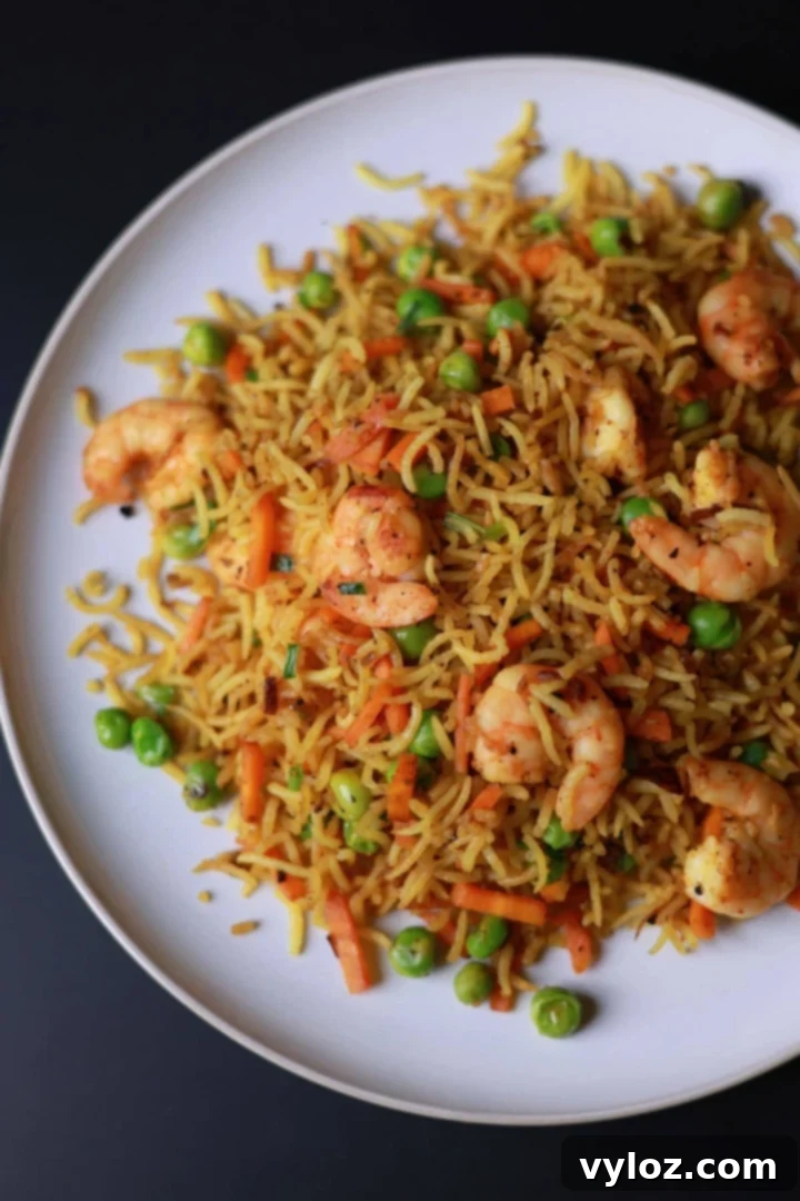 Curry fried rice with shrimp served on a white plate, garnished with fresh herbs.