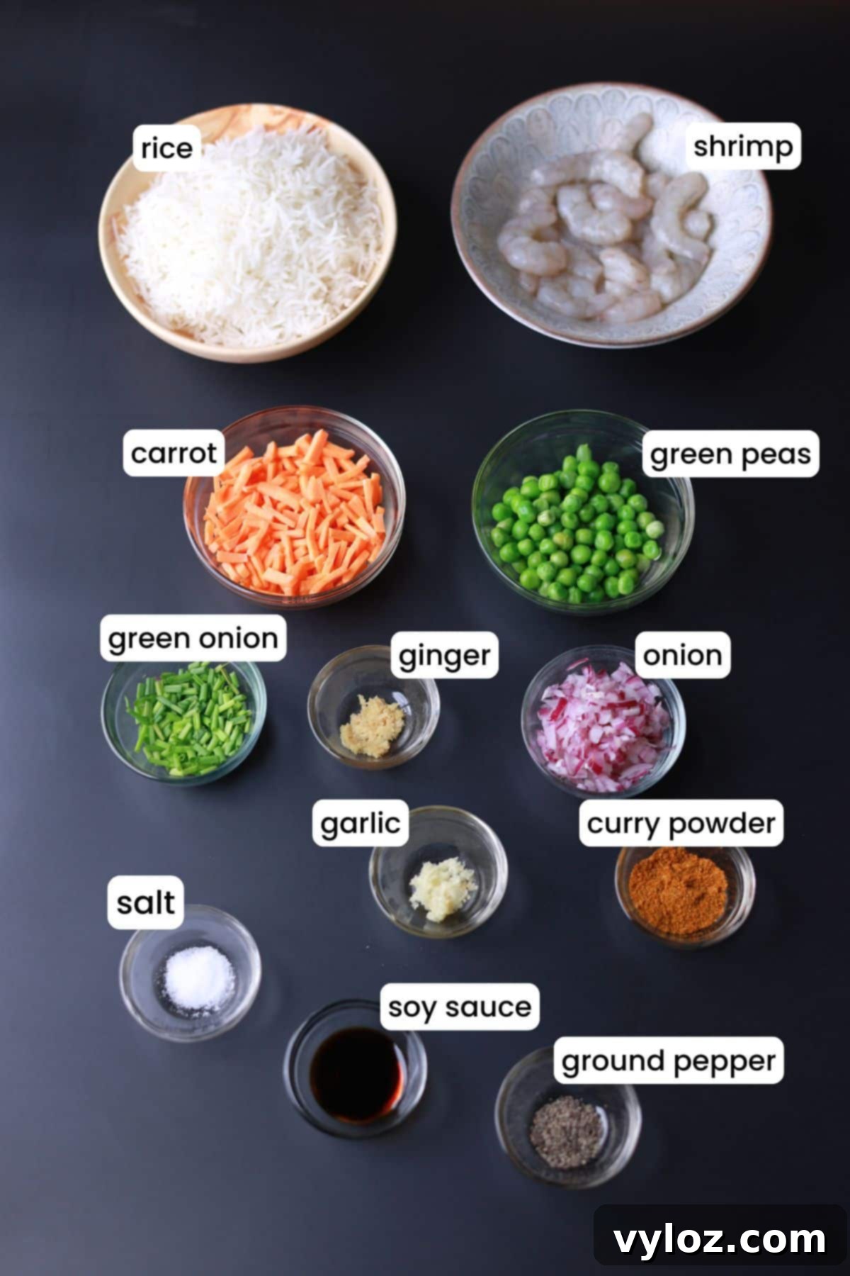 Various curry fried rice ingredients laid out on a black background, including shrimp, rice, vegetables, and spices.