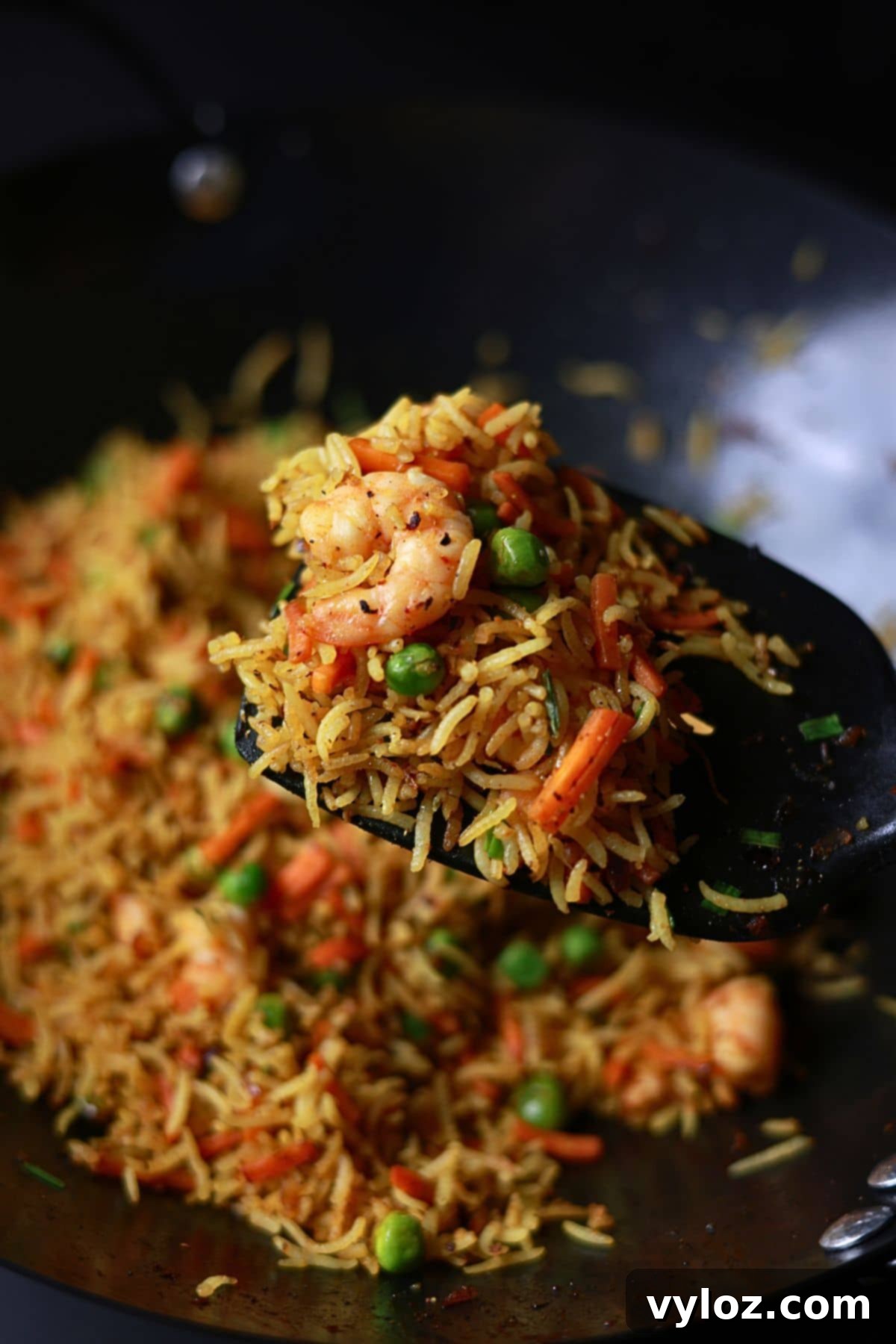 A spatula holding a serving of curry fried rice with shrimp inside a wok, ready to be served.