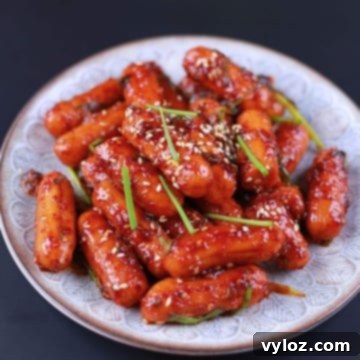 Close-up of spicy sausage stir fry served on a white plate with sesame seeds and green onion.