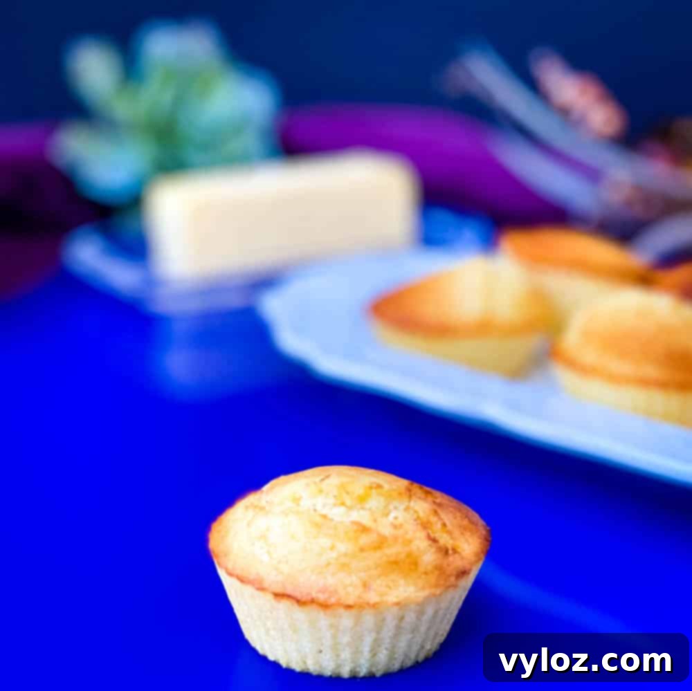 Crispy Air Fryer Cornbread 10 Two beautifully golden air fryer cornbread muffins on a blue plate, with a stack of several more muffins on a white plate in the background.