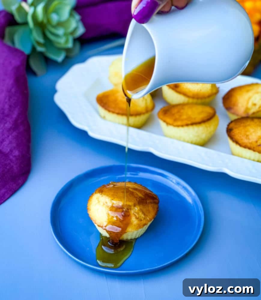 Crispy Air Fryer Cornbread 8 Golden air fryer cornbread muffins on a blue plate, with honey being drizzled, and more muffins on a white plate in the background.