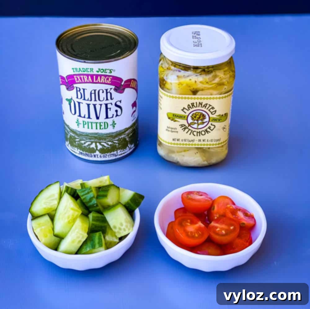 black olives, artichokes, cucumbers, and sliced cherry tomatoes in separate white bowls for antipasto salad recipe