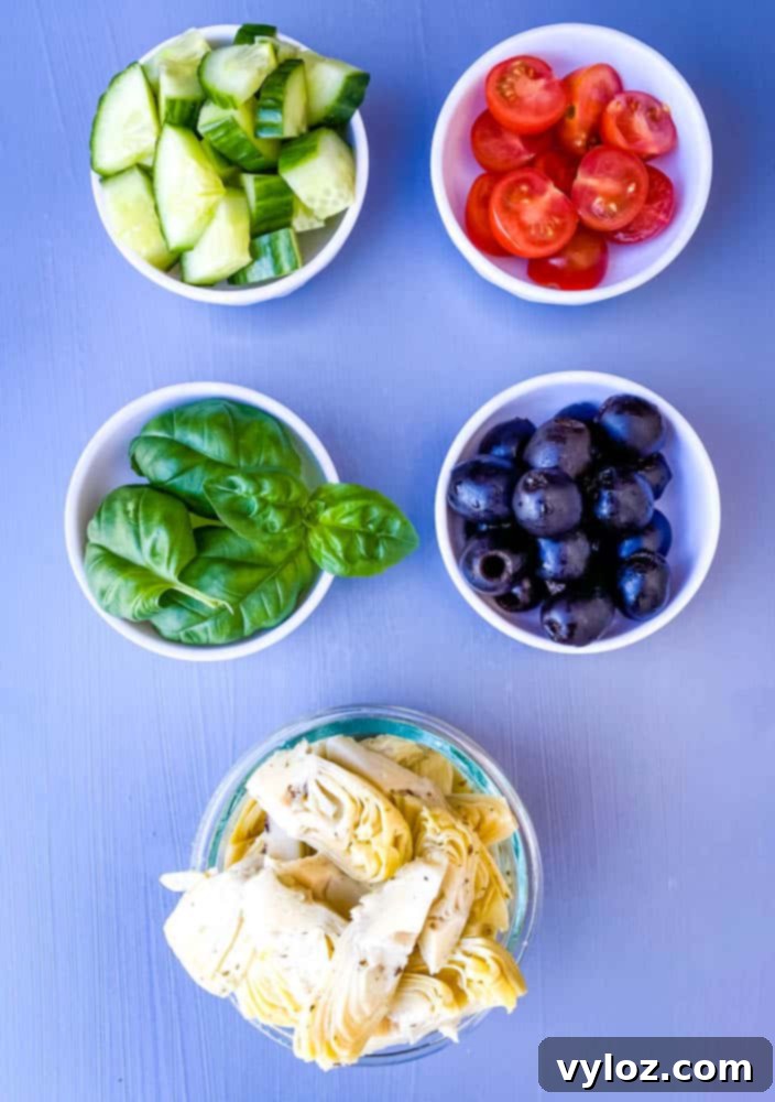 black olives, artichokes, cucumbers, and sliced cherry tomatoes in separate white bowls for antipasto salad recipe