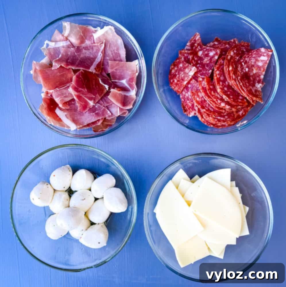 prosciutto, salami, mozzarella balls, and sliced provolone cheese in separate white bowls for antipasto salad recipe