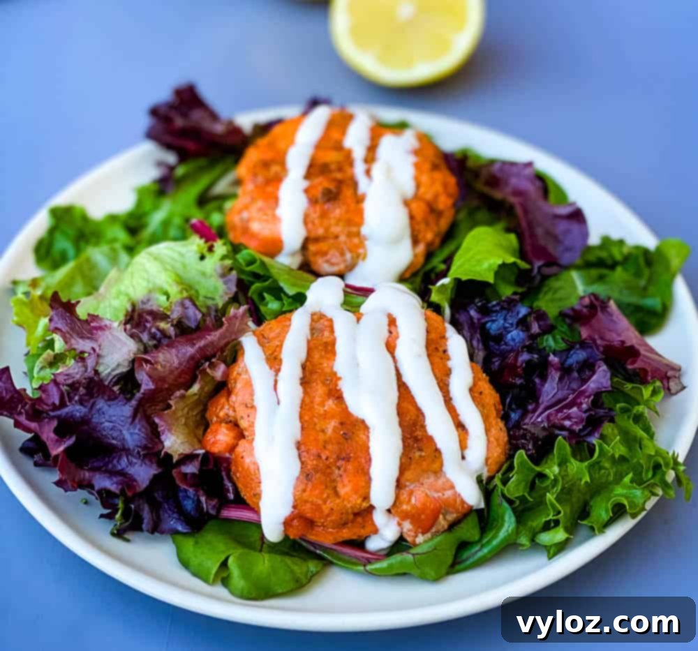 keto low carb salmon patties on a plate with mixed greens and creamy garlic sauce