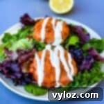 fresh salmon patties on a plate with mixed greens and creamy garlic sauce