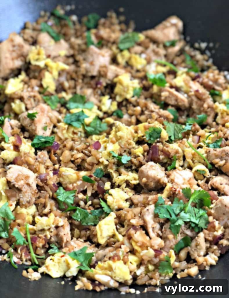 Freshly cooked Keto Low-Carb Cauliflower Chicken Fried Rice garnished with vibrant green onions and a fresh lime wedge, ready to serve