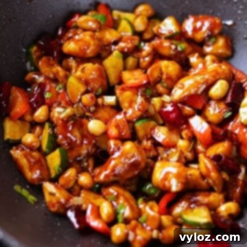 Kung pao chicken coated in a glossy sauce with veggies, peanuts, and dried red chilies.