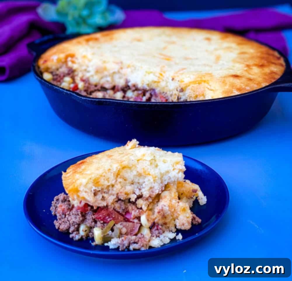 A perfectly portioned slice of tamale pie sits next to the remaining casserole in a cast iron skillet, showcasing its layers.