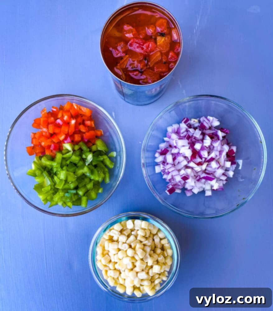 Individual bowls of diced tomatoes, red bell pepper, green bell pepper, chopped onions, and corn, prepared for the casserole filling.