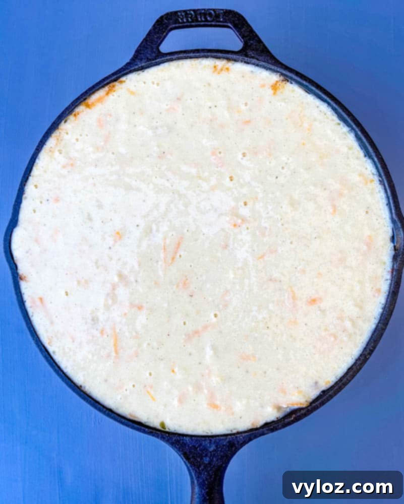 Smooth cornbread batter artfully spread over the rich tamale pie filling in a cast iron skillet, ready for baking.