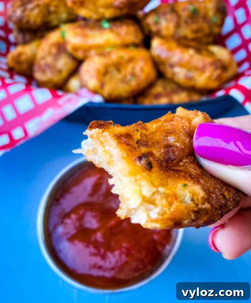 Person holding an air fryer tater tot with a bite taken out, showing the crispy exterior and fluffy interior