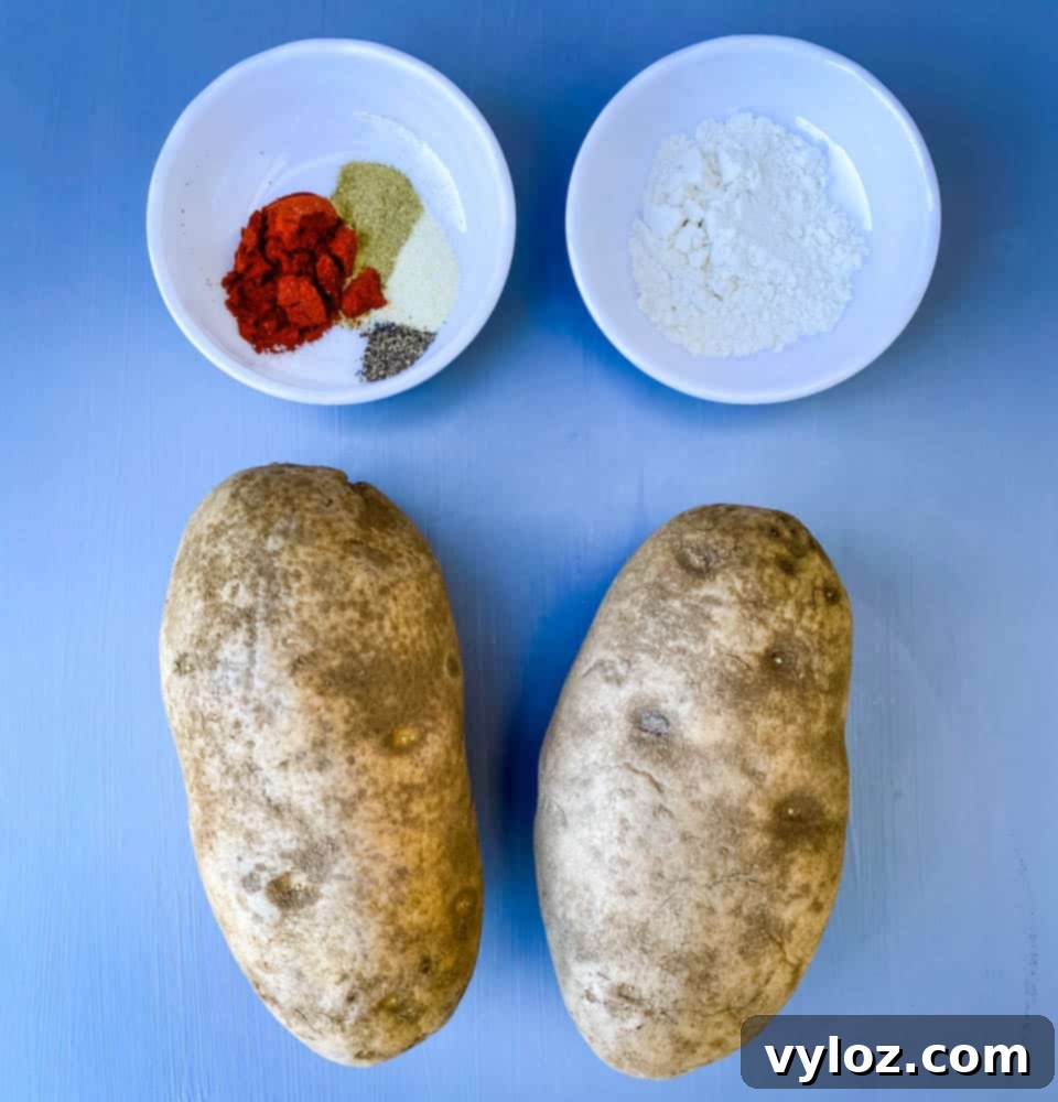 Two russet potatoes on a flat surface next to a sprinkle of flour and seasoning, ready for homemade tater tots