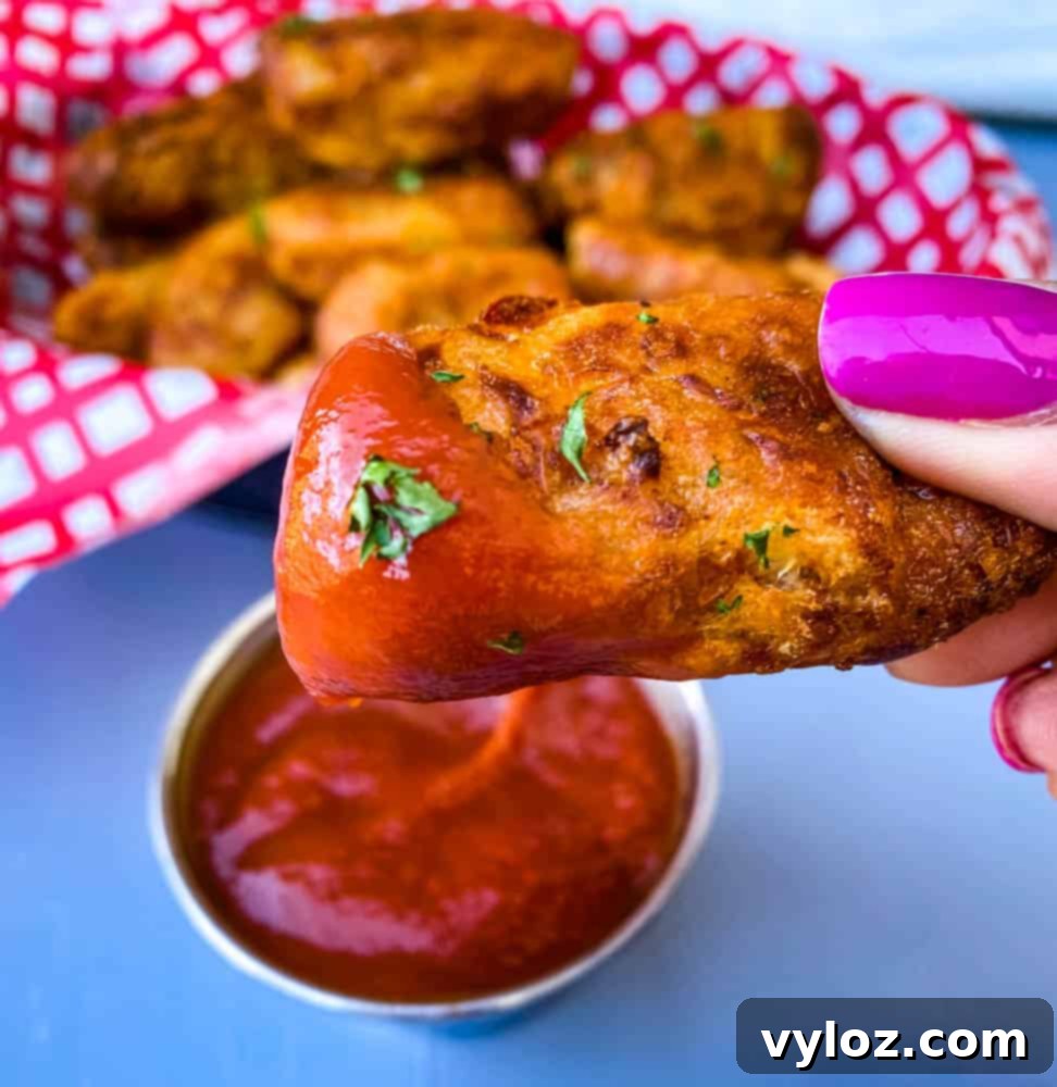 Person holding an air fryer tater tot dipped in ketchup