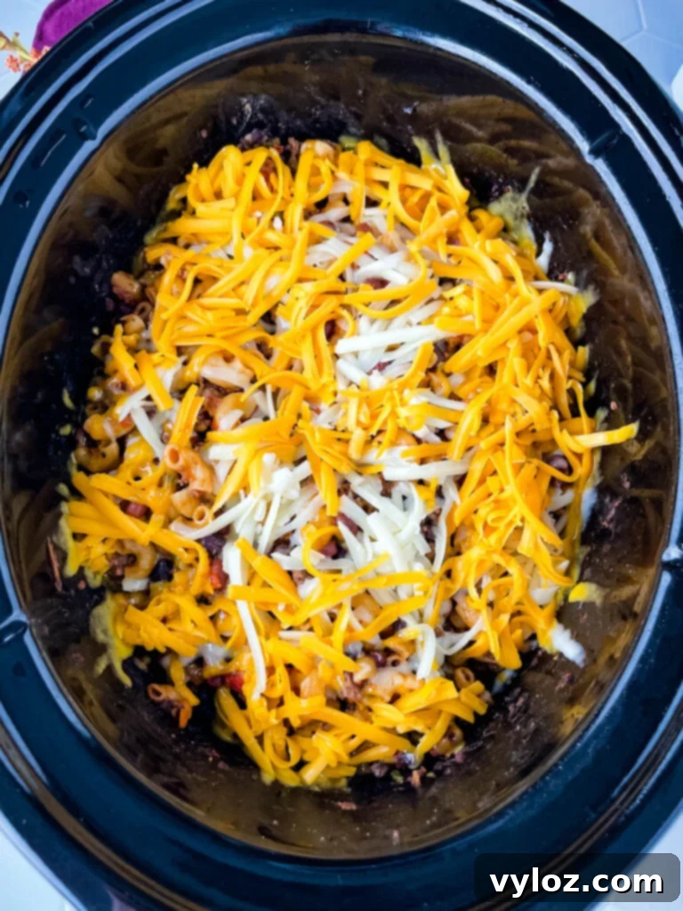 Ultimate Slow Cooker Chili Mac and Cheese 8 uncooked chili mac and cheese in a slow cooker topped with cheese