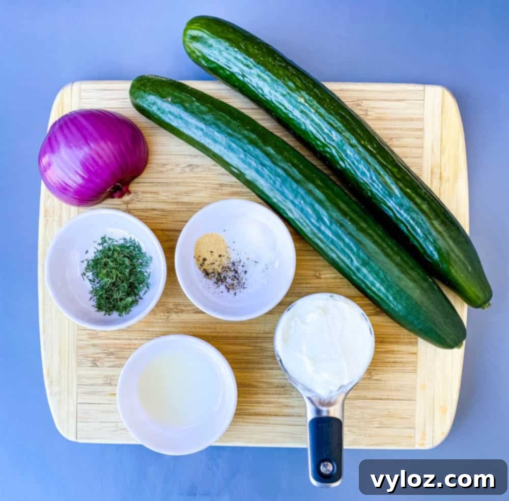 fresh cucumber and a red onion on a bamboo cutting board with a cup of Greek yogurt, fresh dill, seasoning, and lemon juice in separate bowls