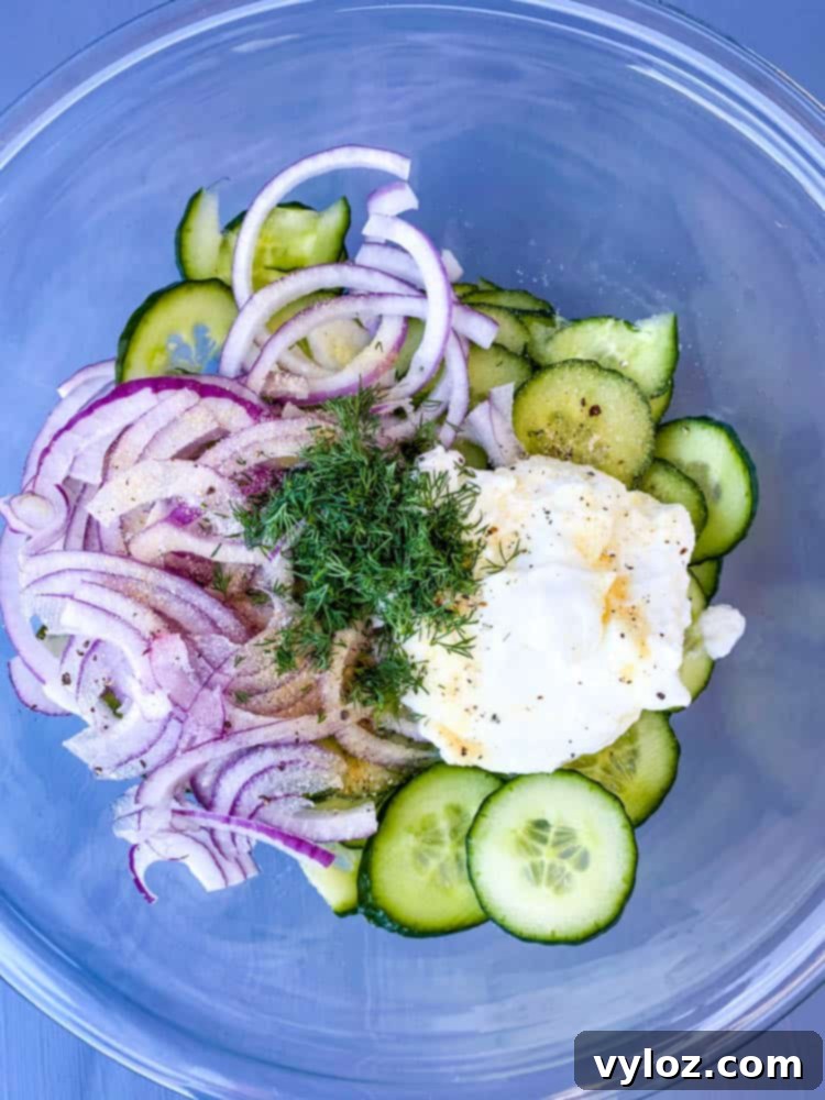 sliced cucumbers and onions in a glass bowl with Greek yogurt, lemon juice, seasoning, and fresh dill