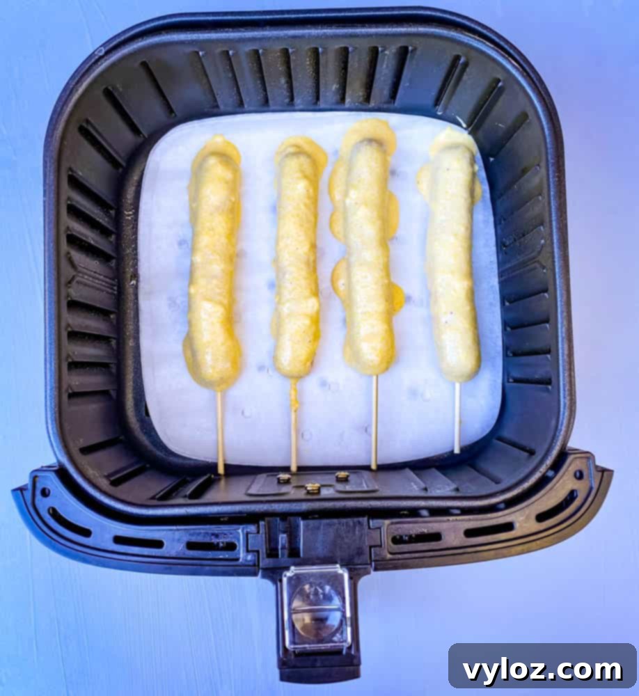 uncooked corn dogs arranged in an air fryer basket, ready to be cooked to perfection