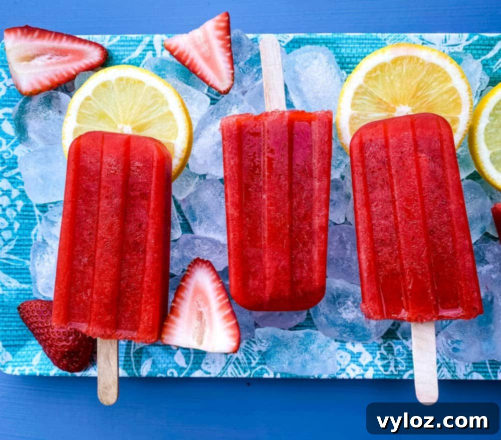 sugar free strawberry lemon popsicles on a flat surface with ice, fresh lemons and strawberries