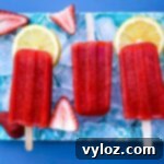sugar free strawberry lemon popsicles on a flat surface with ice, fresh lemons and strawberries