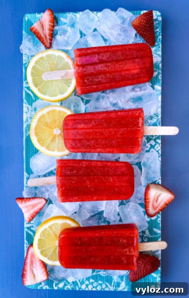 sugar free strawberry lemon popsicles on a flat surface with ice, fresh lemons and strawberries