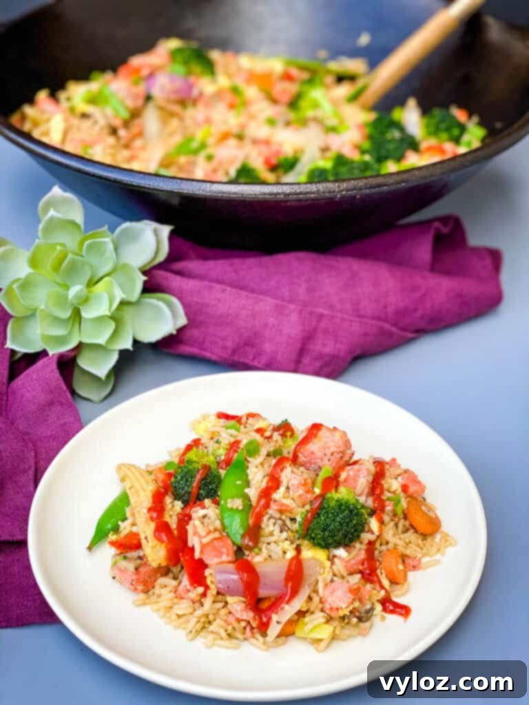 a white plate of salmon fried rice drizzled with hot sauce a wok filled with fried rice