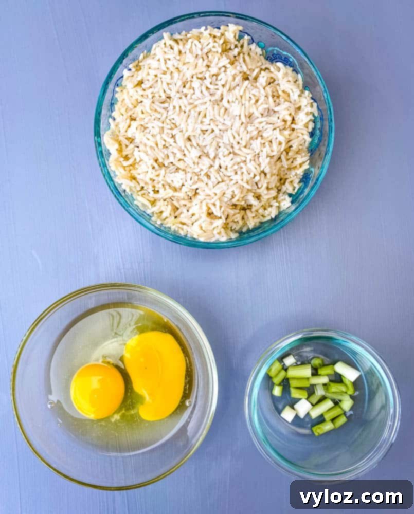 cooked and cold brown rice, raw eggs, and green onions in separate bowls