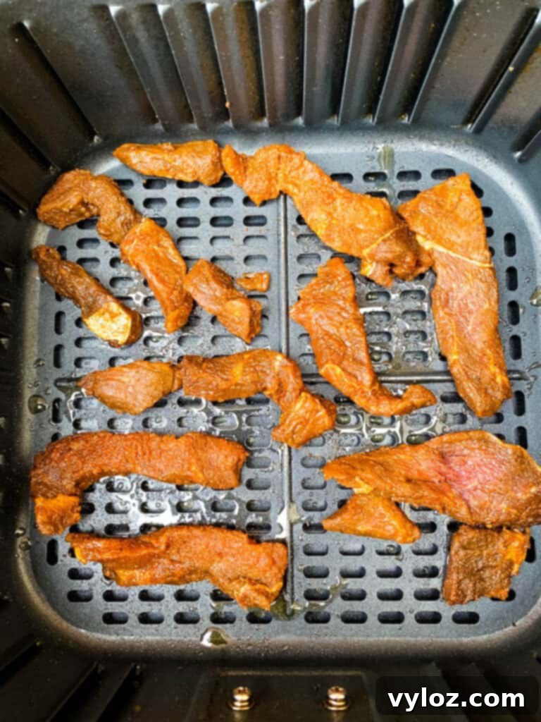Several pieces of beef jerky lying flat inside an air fryer basket, dehydrating