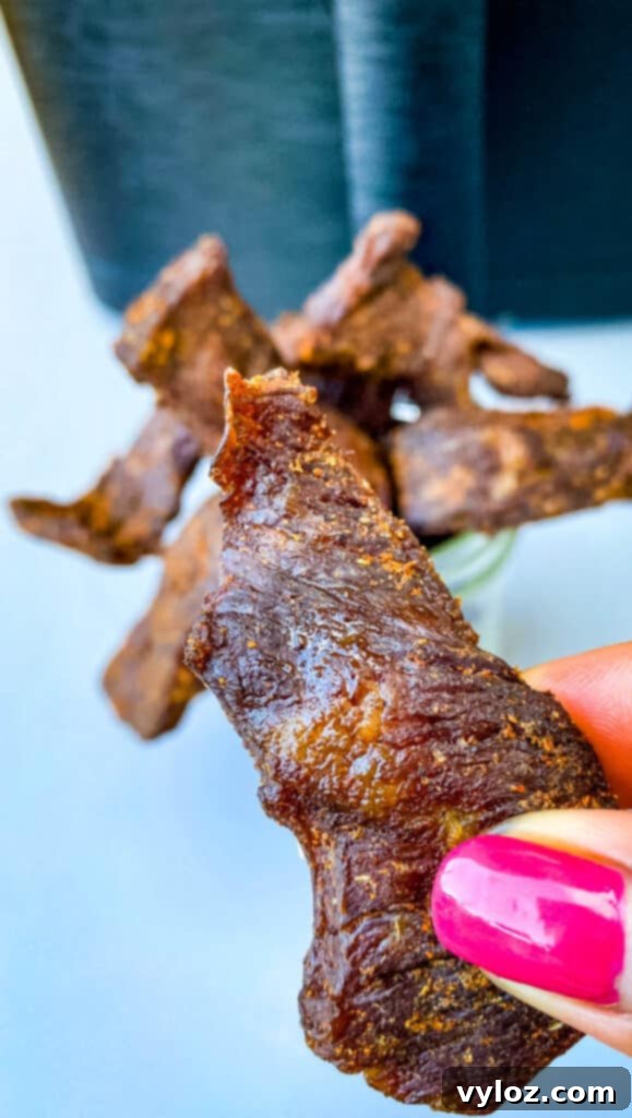 A hand holding a piece of air fryer beef jerky, showcasing its texture and golden-brown color