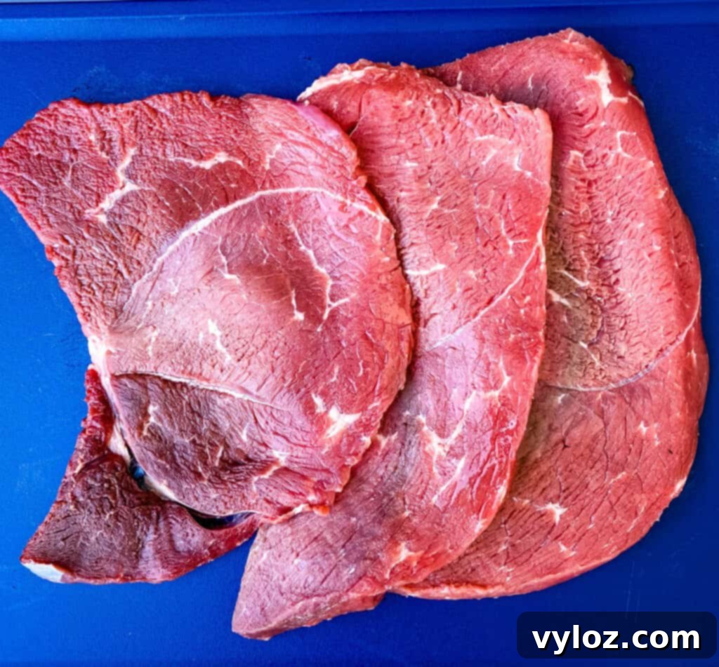 A raw sirloin tip steak on a wooden cutting board, ready for slicing.