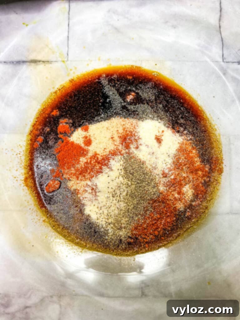 Close-up of a glass bowl filled with a rich, dark marinade, featuring soy sauce, liquid smoke, and worcestershire sauce