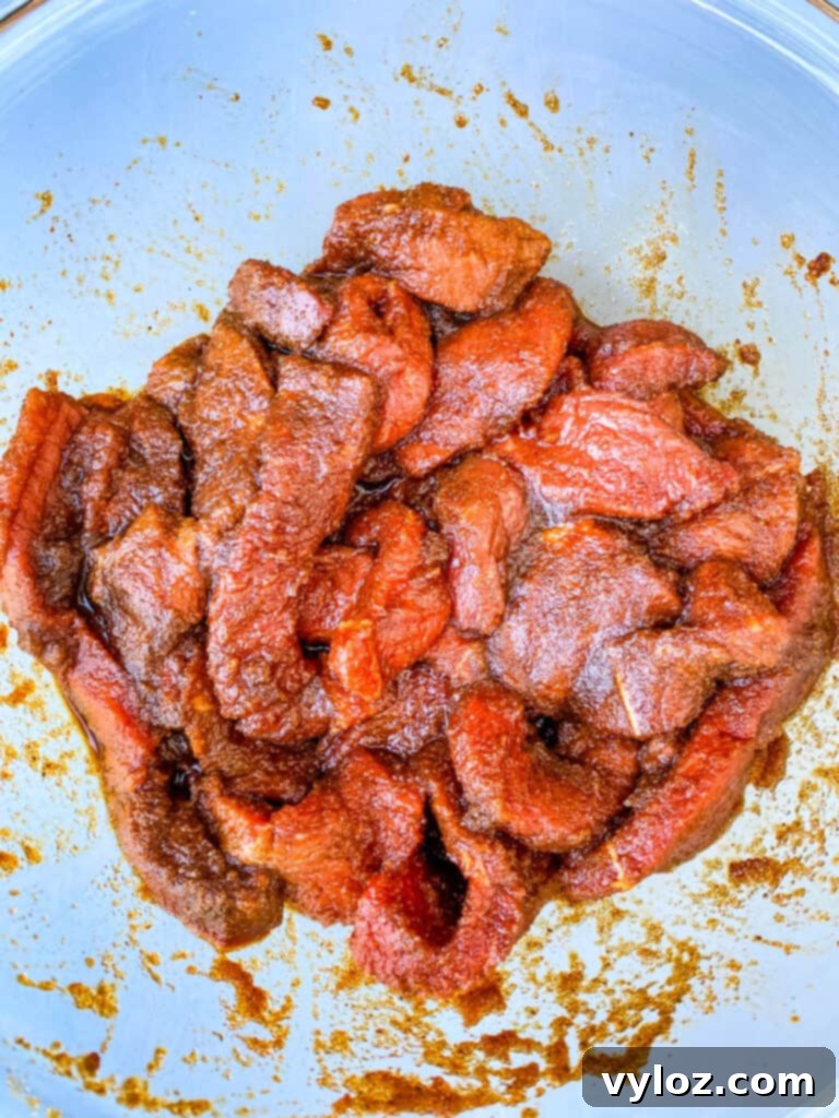 Raw marinated beef strips soaking in a rich, dark marinade in a glass bowl